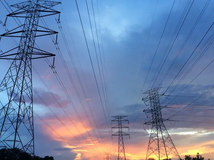 Image of transmission towers against a grey cloudy sky with a yellow sunset at the bottom. Photo by Pok Rie on Pexels